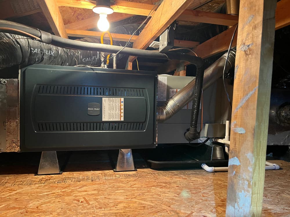 HVAC unit installation in attic with exposed ductwork and lighting.